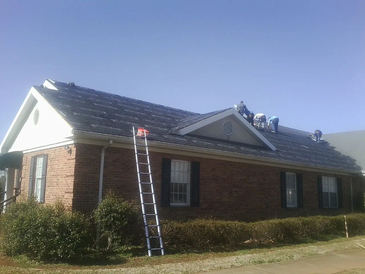 Crew tearing shingles off a brick ranch roof with a ladder set — Metal Roof Repair work by our crew in Tuscarora