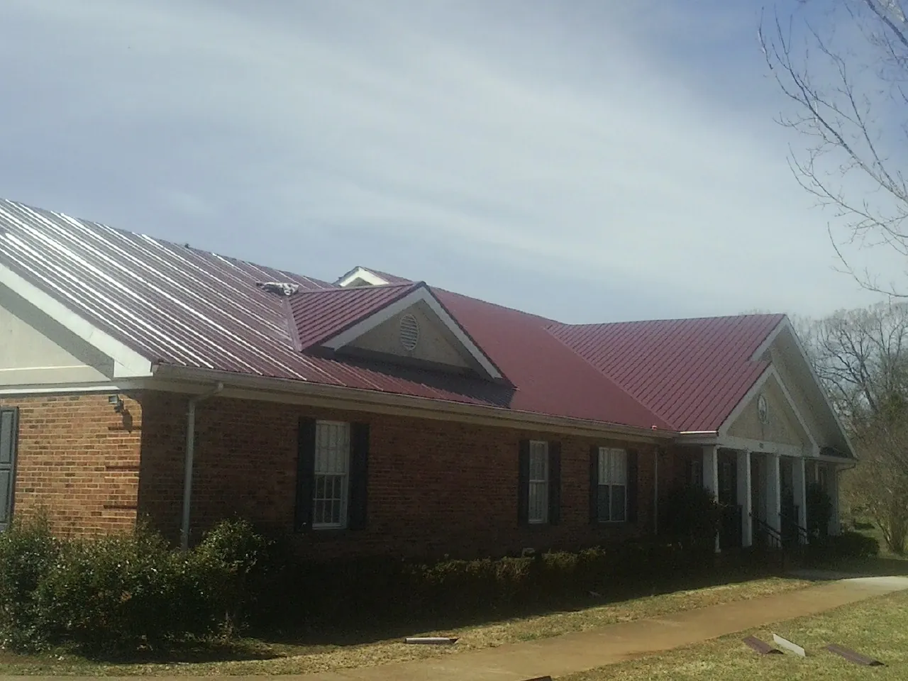 Red metal roof with gabled entries on a long brick building, from a Hail Damage Roof Repair job in Tuscarora
