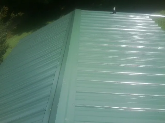 New green metal panels meeting at the ridge of a roof — Flat Roof Repair work by our crew in Tuscarora