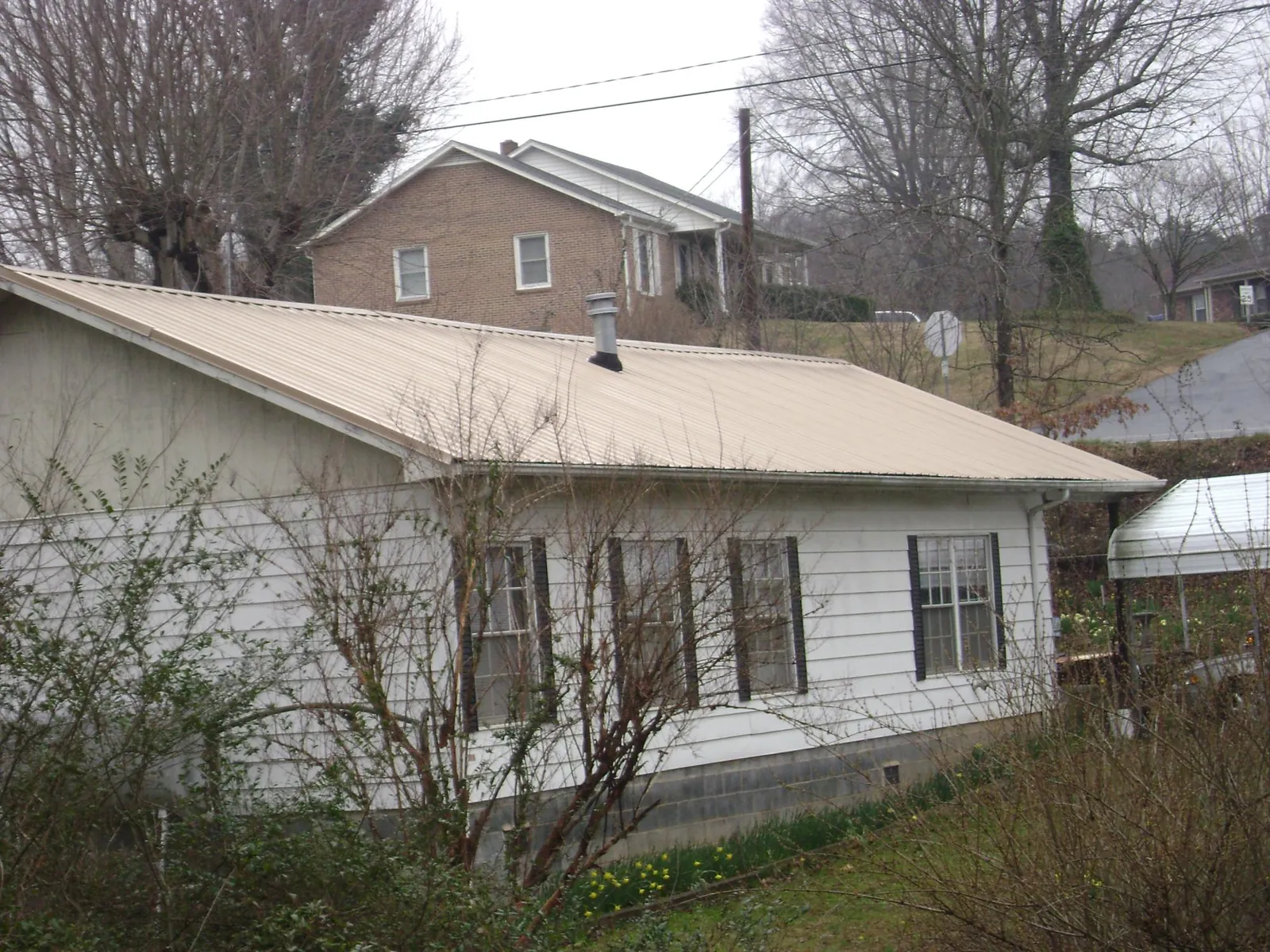 Tan metal roof on a white sided house set into a hillside — Commercial Roofing by Roofing Brothers in Tuscarora